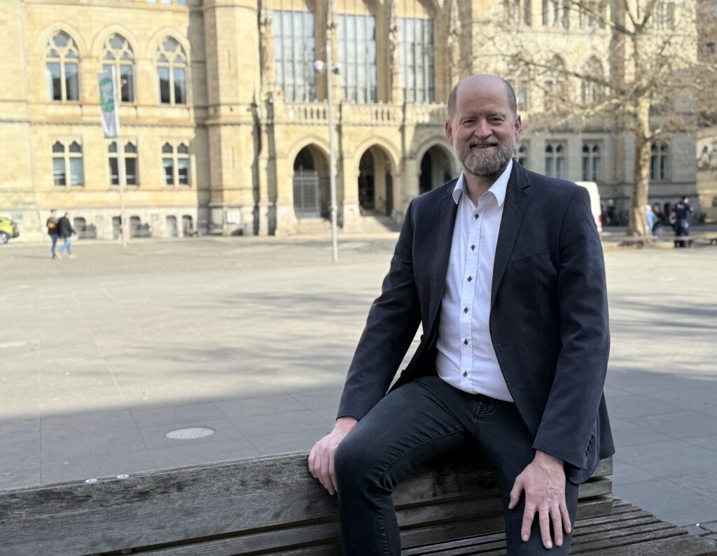 Ingo Schramm sitzt auf der Lehne einer Bank auf dem Platz der Deutschen Einheit, im Hintergrund ist das Braunschweiger Rathaus.